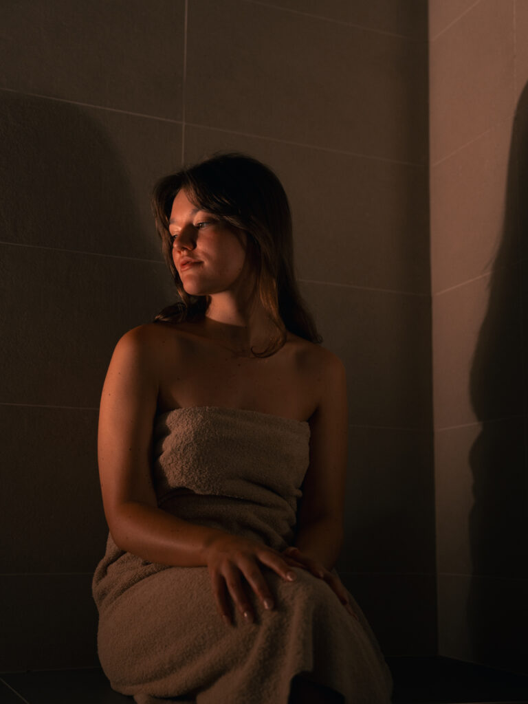 Woman relaxing in a dimly lit sauna wrapped in a towel