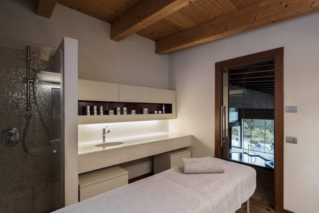 Modern spa room with massage table, shower, and wood ceiling.