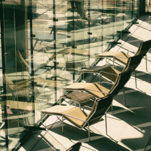 Outdoor seating area with chairs and glass walls near a piscina.