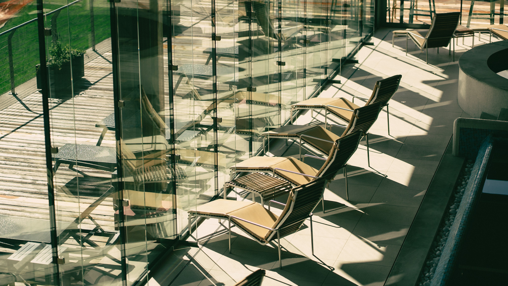 Outdoor seating area with chairs and glass walls near a piscina.