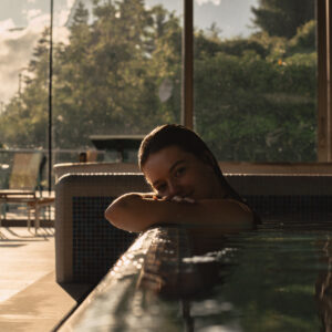 Person relaxing in a pool indoors with sunset view