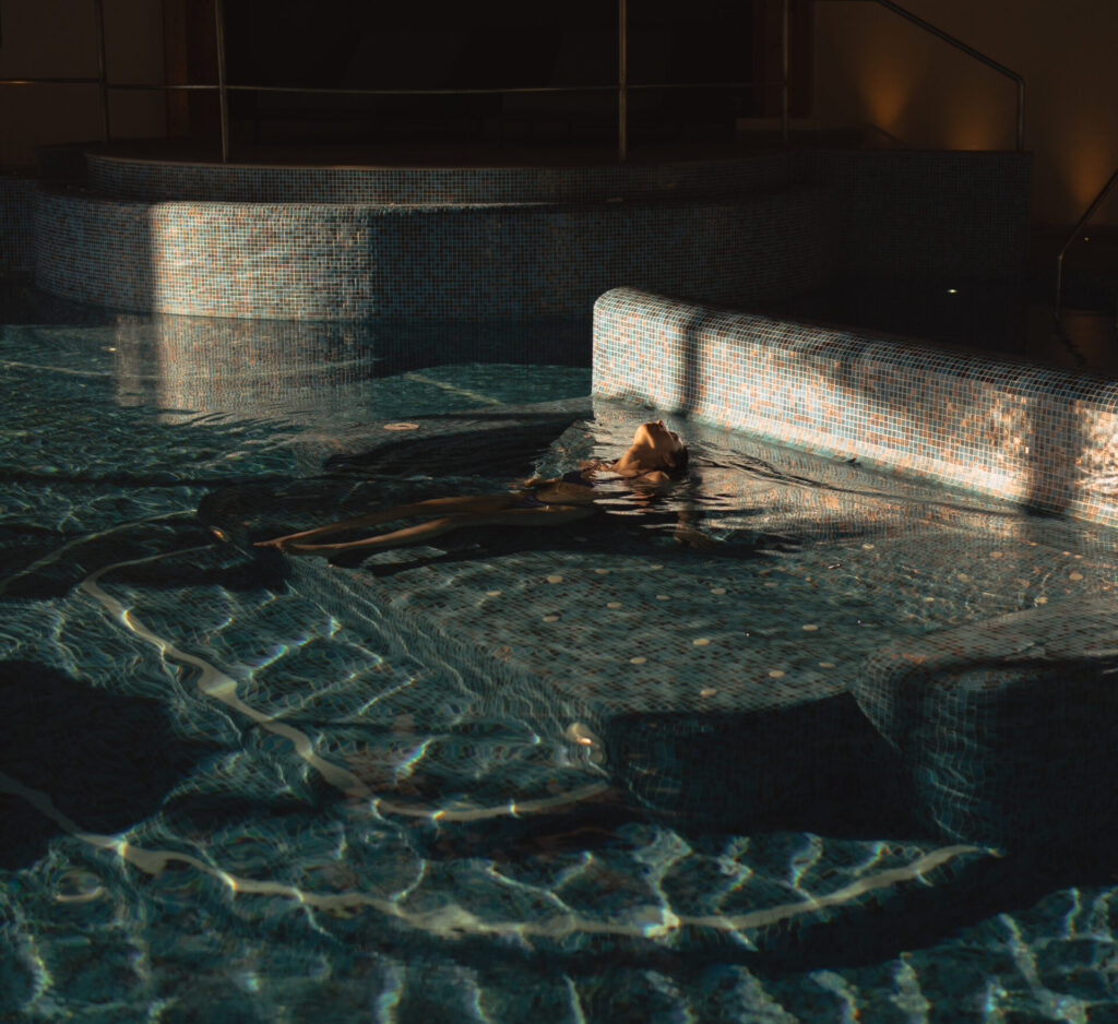 Person relaxing in a modern indoor pool with moody lighting