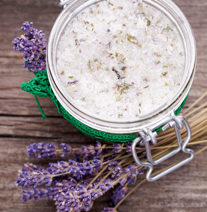 Jar of lavender bath salts with fresh lavender sprigs on a wooden surface.