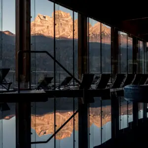 Indoor pool reflects mountain view through large windows, lounge chairs nearby.