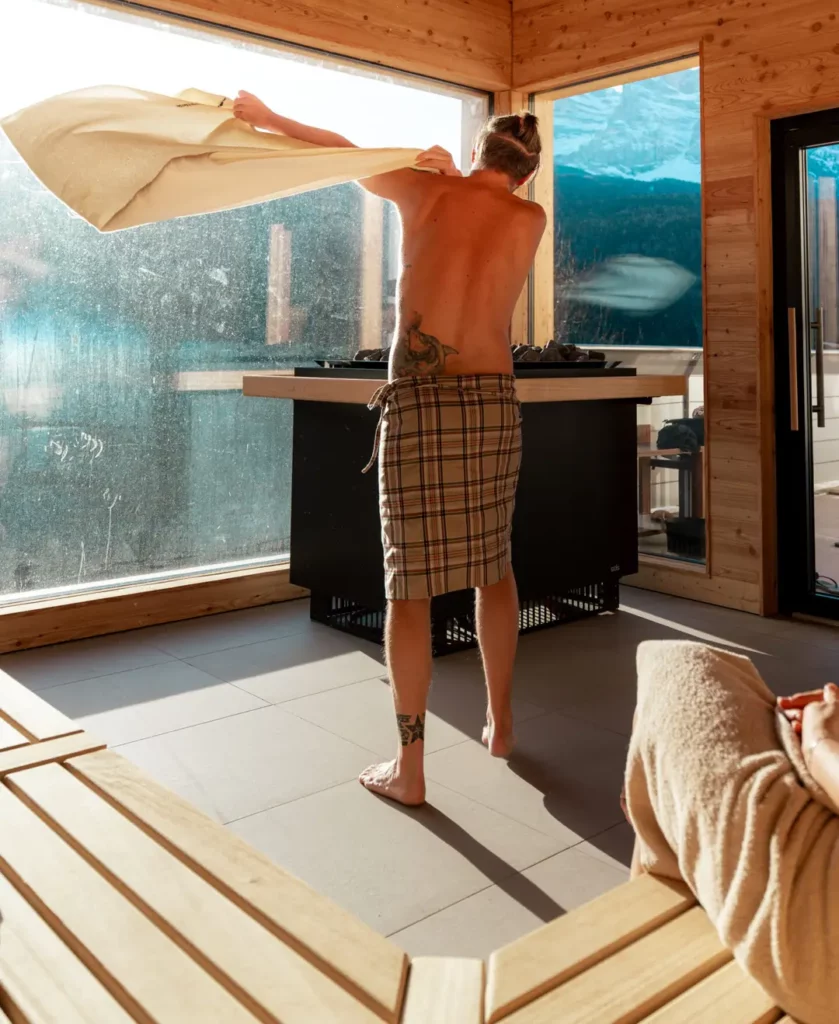 Man in sauna with towel, back view. Wood interior, relaxing spa day.